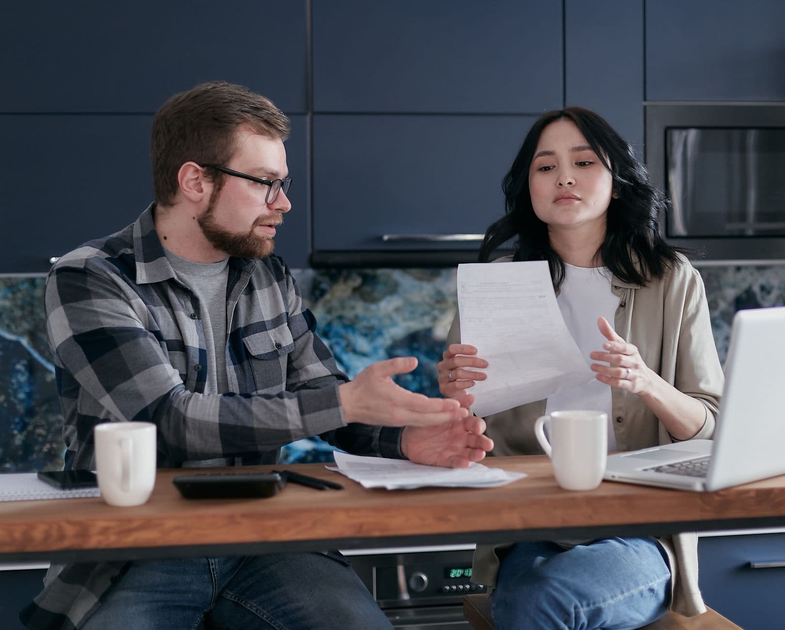 A parent reviewing paperwork and a laptop at a kitchen table