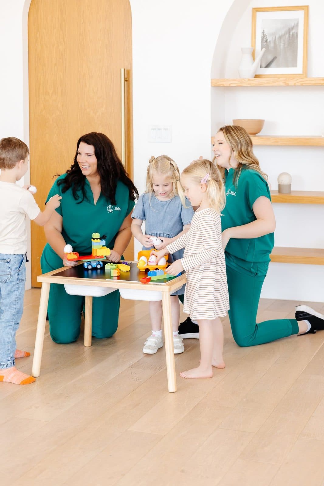Children playing with toy eggs and building blocks with two female caregivers