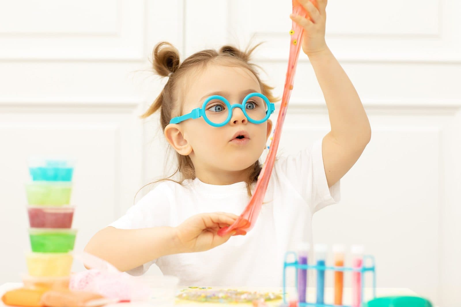 Young girl wearing large blue glasses holding slime with colorful containers, working on sensory and motor skills during occupational therapy for kids in Houston, TX
