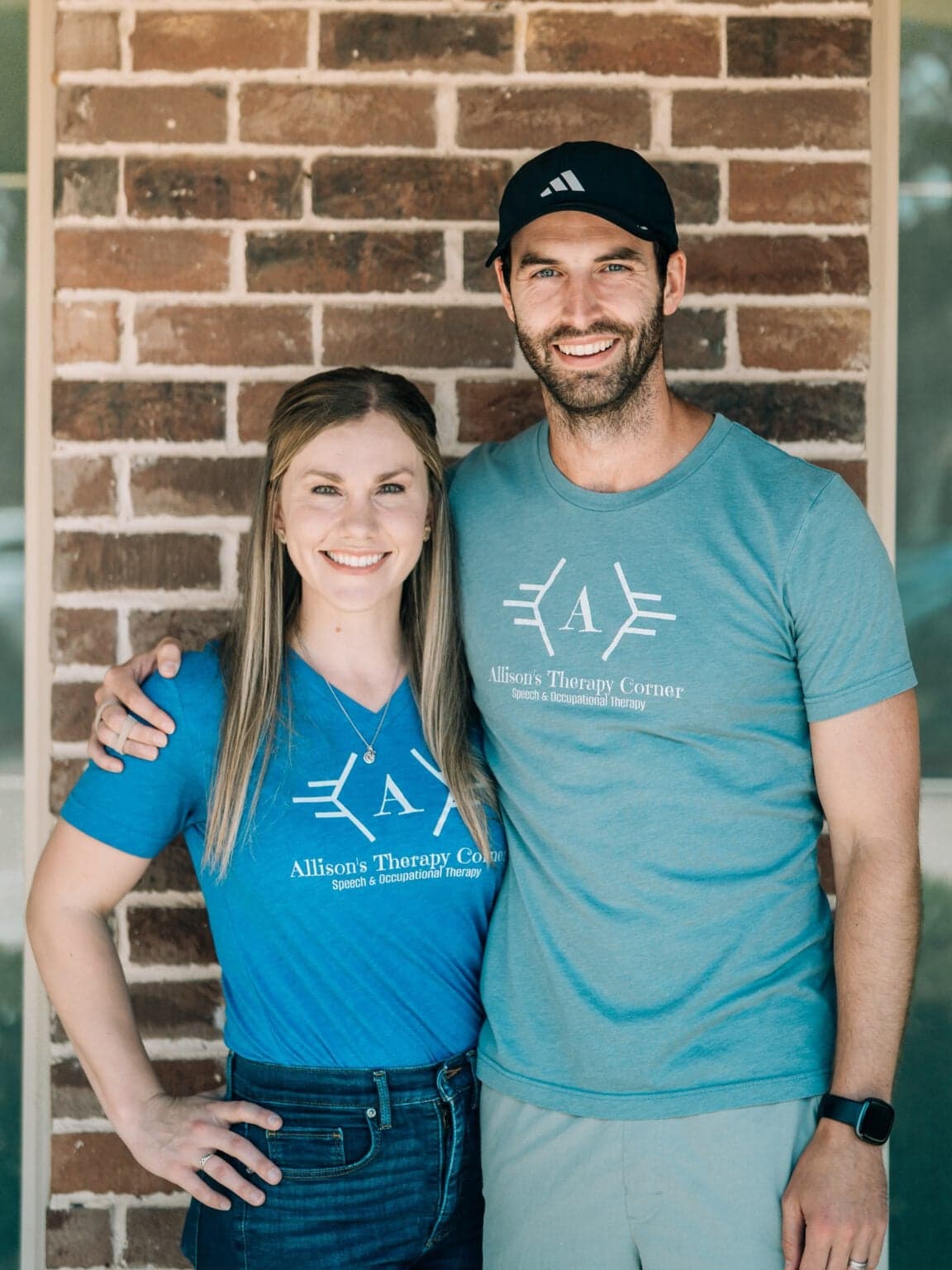 Owners of Allison's Therapy Corner standing together wearing branded shirts outside the clinic.
