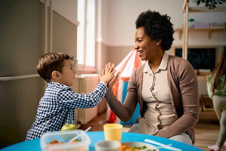 a woman is giving a child a high five while sitting at a table
