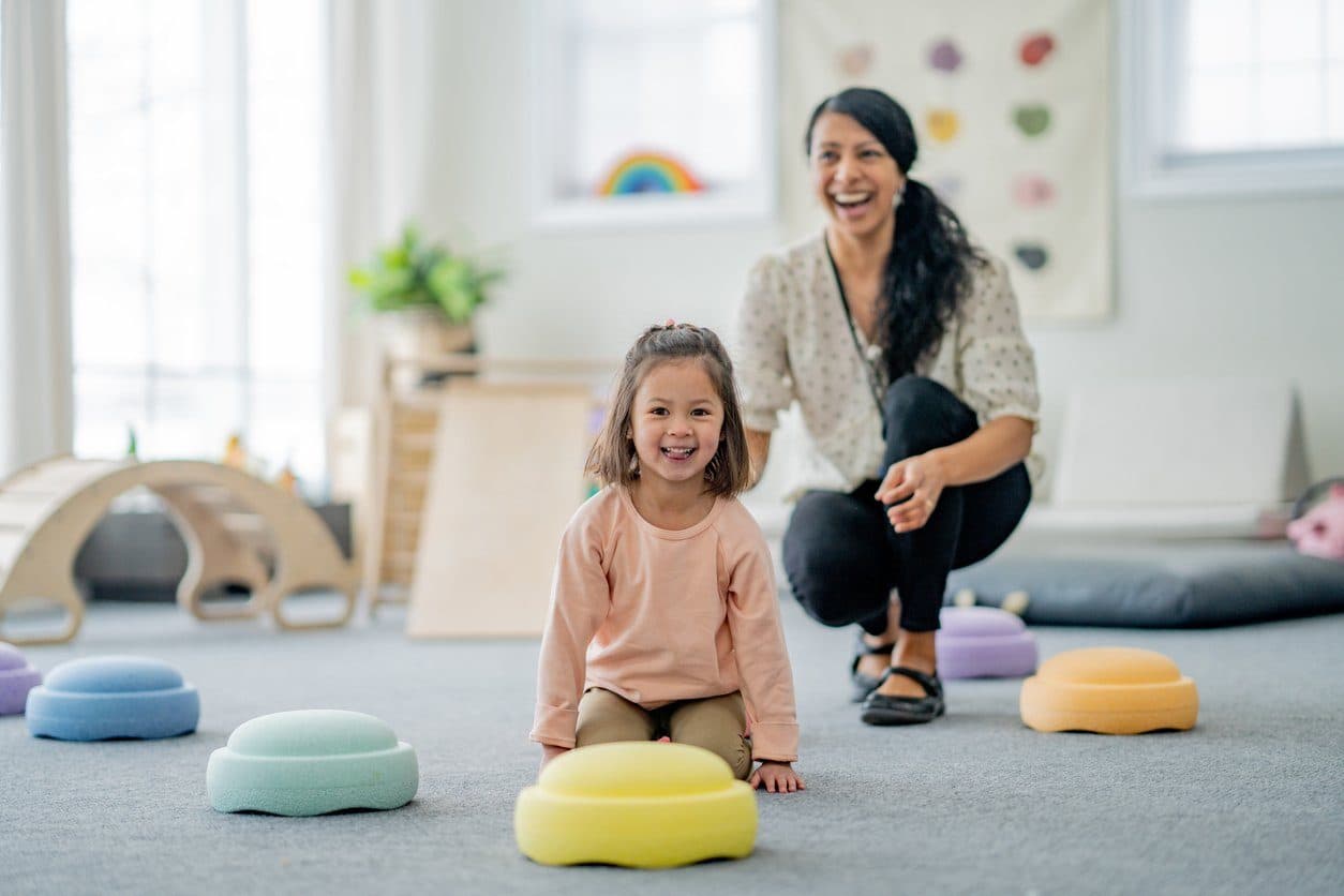 A young girl working on motor and sensory skills with an OT in a playroom with colorful cushions during occupational therapy for kids in Houston, TX