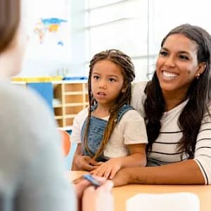 a woman and a little girl are sitting at a table talking to a teacher