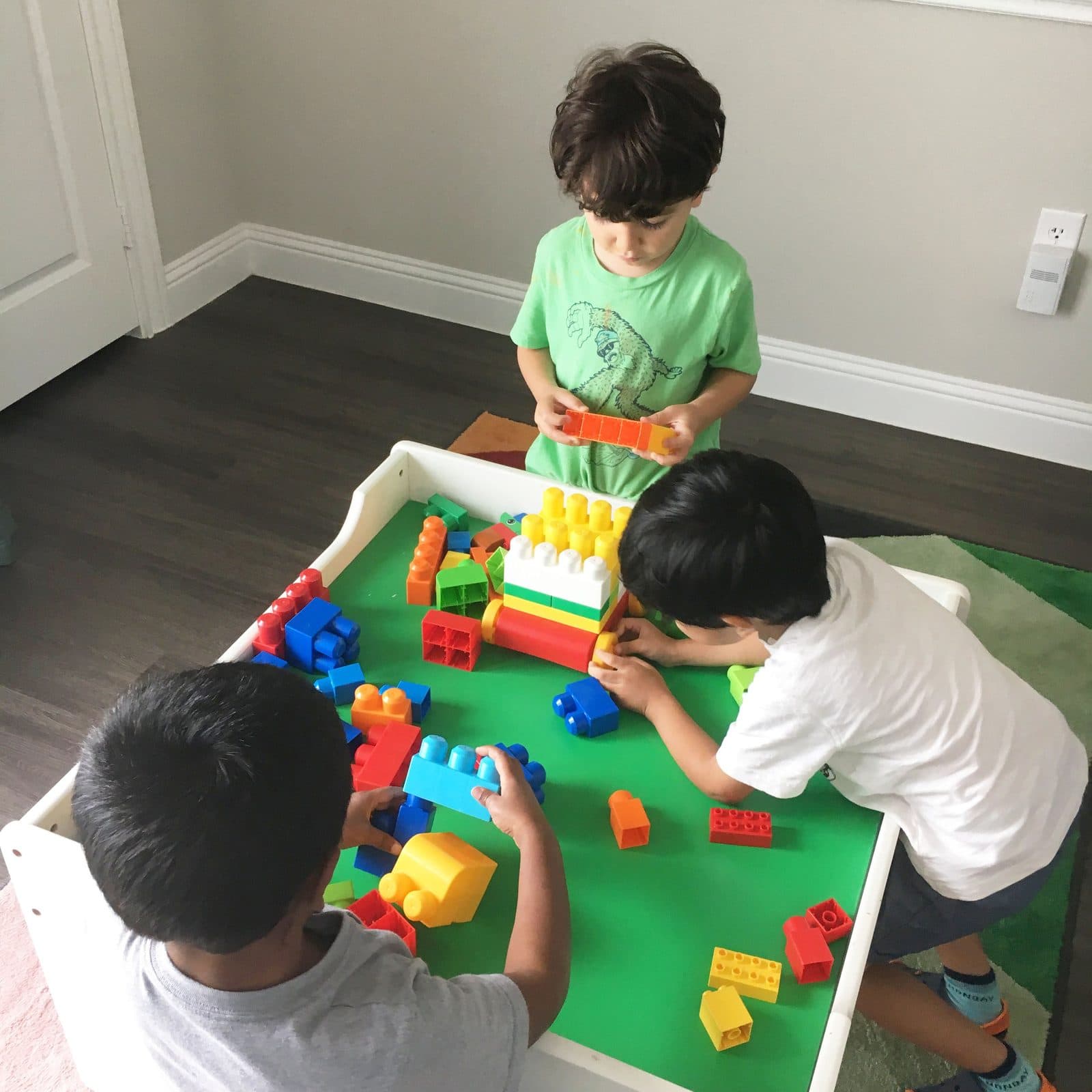 Three children playing with colorful plastic building blocks in the social group program