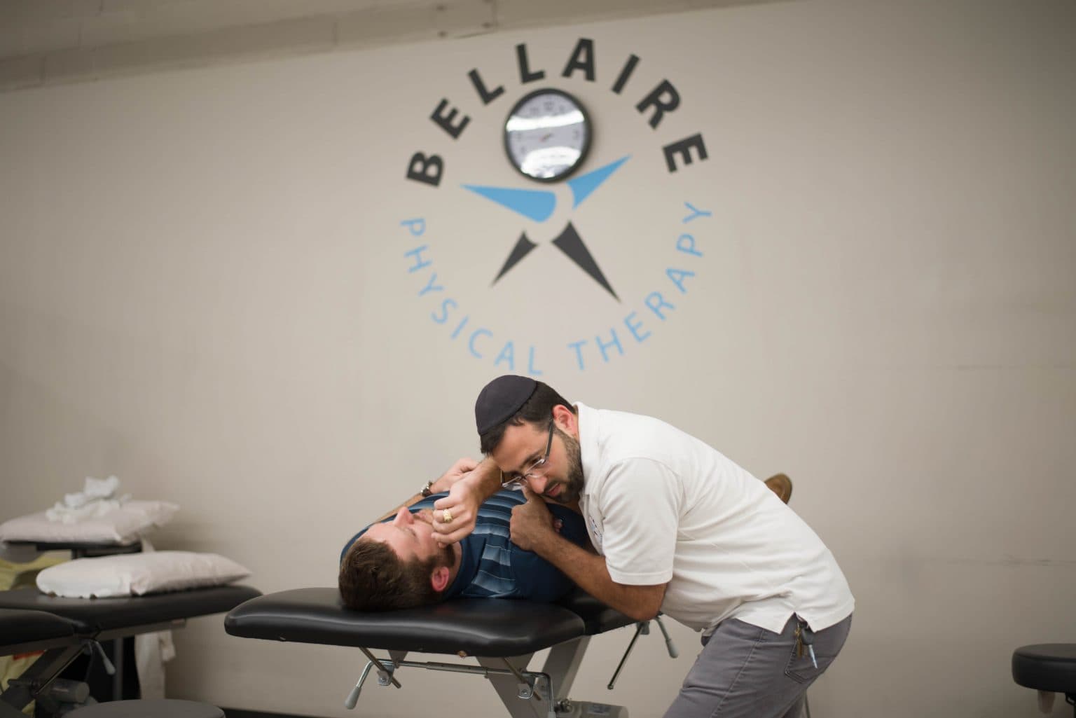 Wider view of therapist performing manual therapy on patient in Bellaire Physical Therapy clinic with multiple treatment tables visible