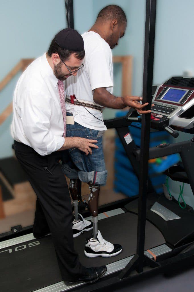 Physical therapist assisting patient with prosthetic leg on treadmill in therapy gym
