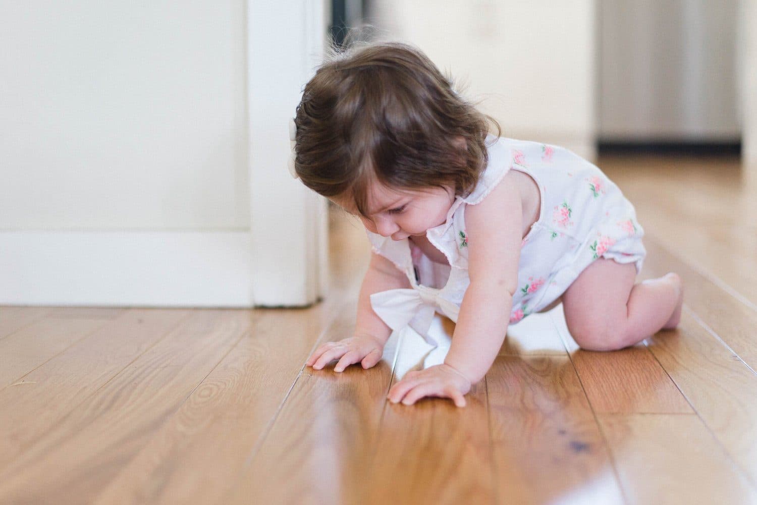 A young girl crawling on a hardwood floor, looking distressed.