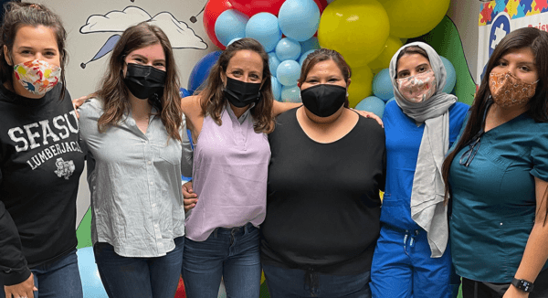 Six people with masks pose for a photo in front of balloons, smiling