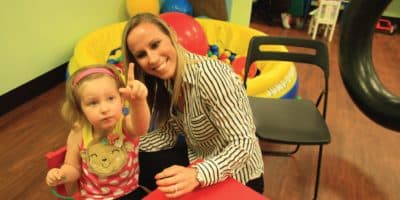 Therapist and child in colorful therapy room with donut-shaped foam equipment and ride-on toys