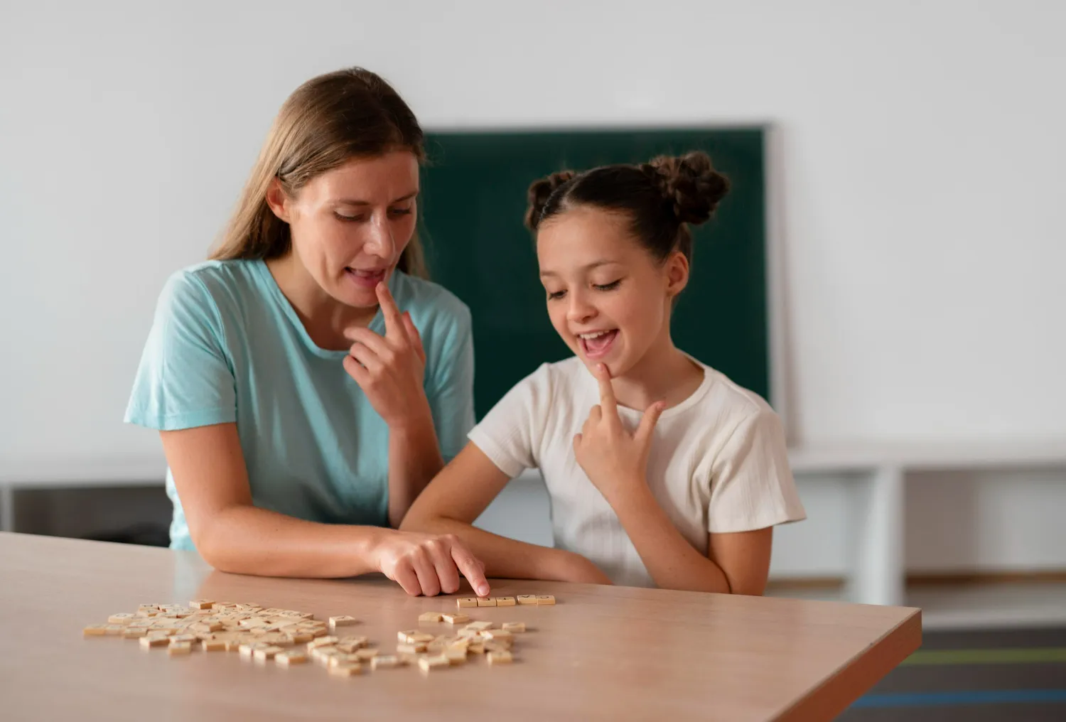 Woman and girl sitting at a table pointing at letter tiles, practicing speech or reading